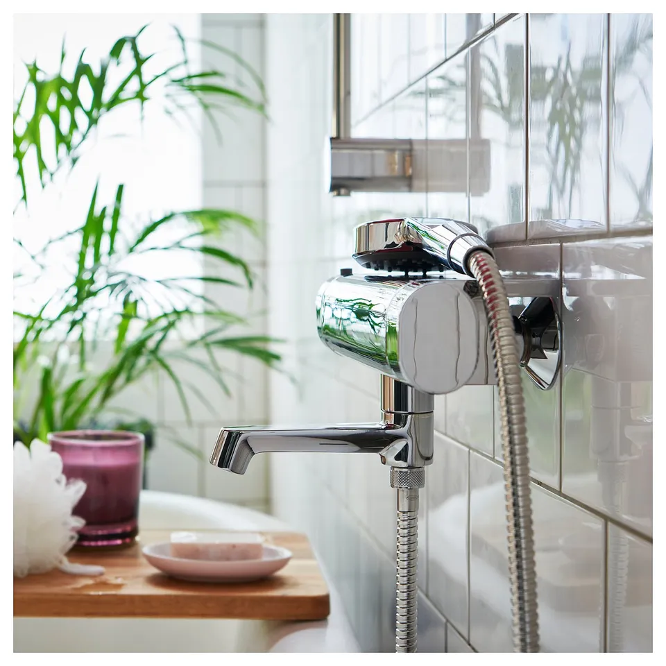 Modern chrome shower head with flexible hose attached to wall. Plant and decorative items nearby.