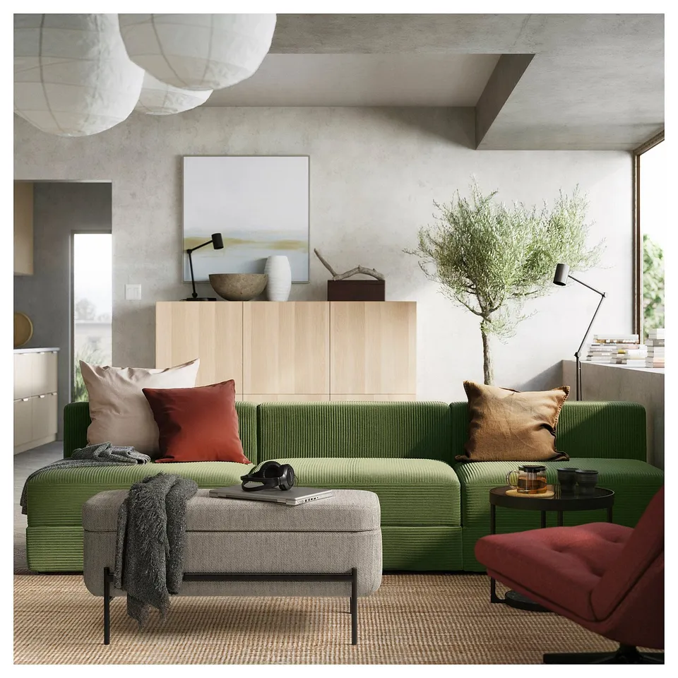 Modern living room with green VALTORP sofa, red chair, wooden cabinet, and hanging lamps.