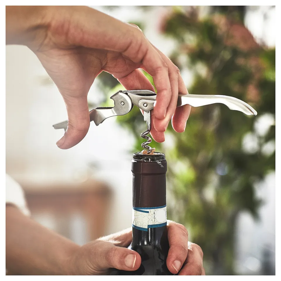 Person using a silver SEGELFISK corkscrew to open a wine bottle. Easy to grip design, stainless steel material.