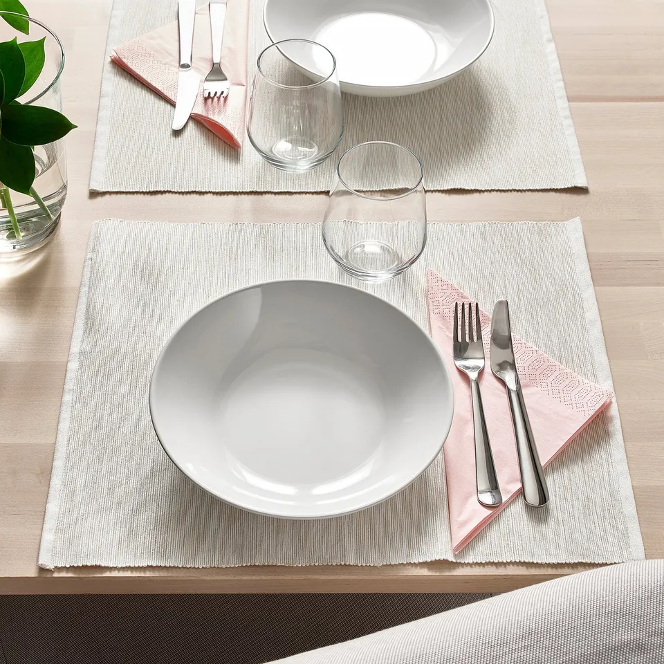 Two table settings with white dishes, glasses, and silverware on white woven placemats.