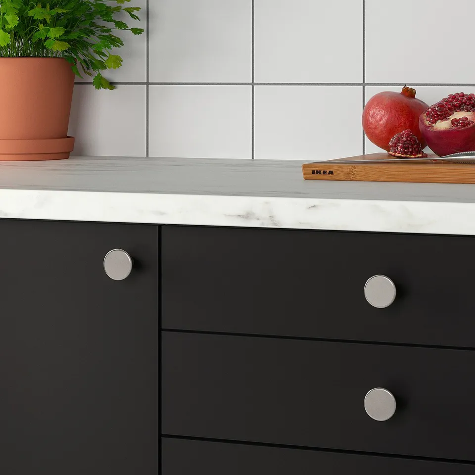 Modern kitchen countertop with dark cabinets and marble surface. Displayed are pomegranates on a cutting board and a plant.