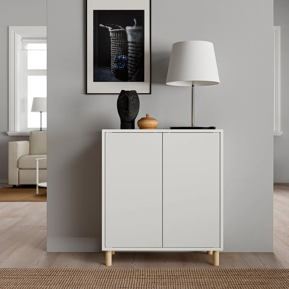 Modern living room EKET white cabinet with wooden legs, table lamp, sculpture, and framed art.