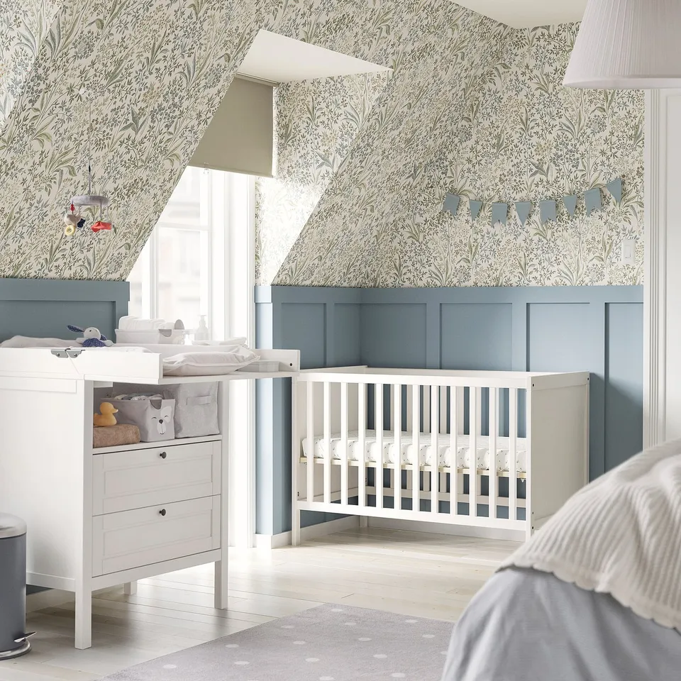 Nursery with light blue SUNDVIK cot and changing table, floral wallpaper.