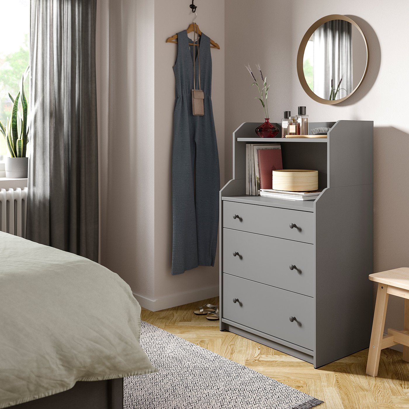 Bedroom with modern decor, featuring a grey HAUGA dresser, hanging blue dress, round mirror, and potted plant.