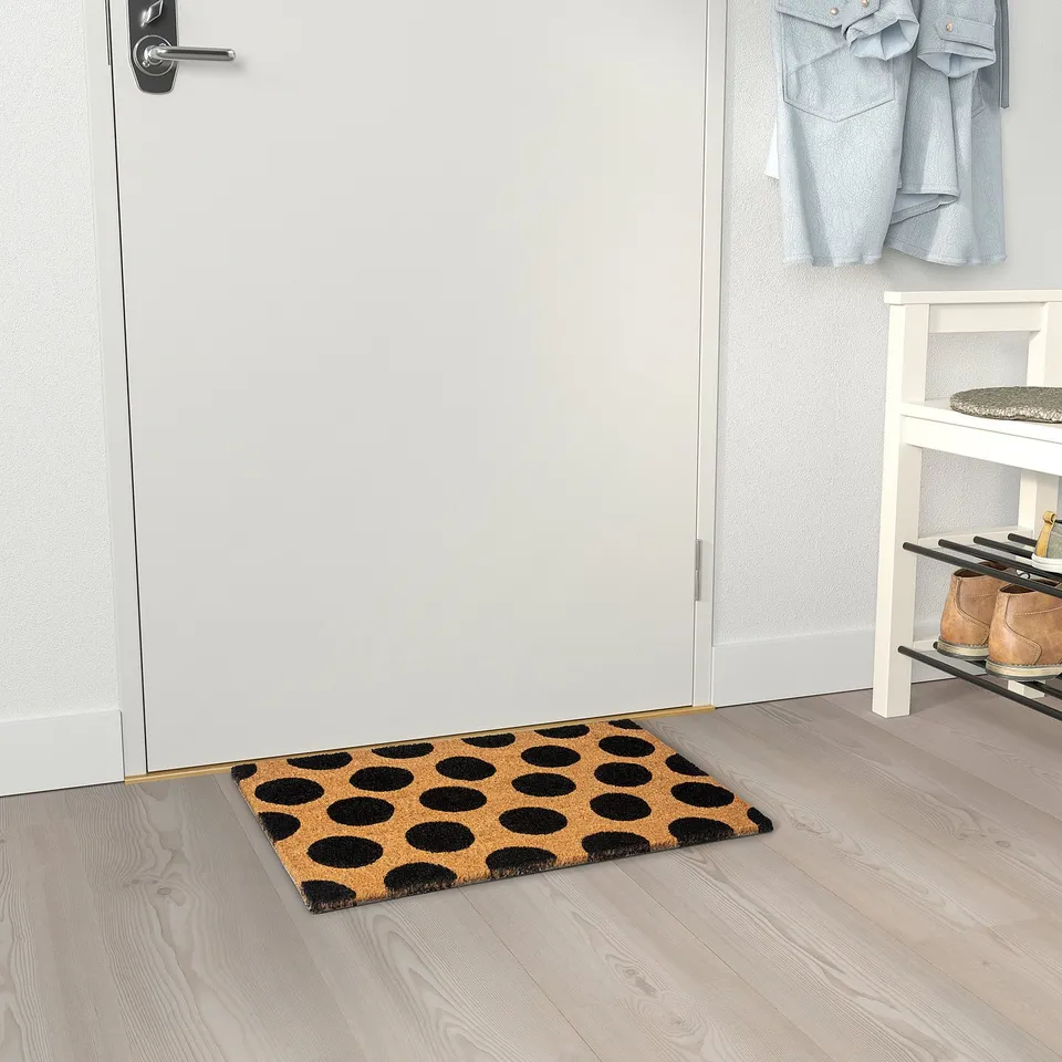 Black dot doormat by shoe rack, fits under door.