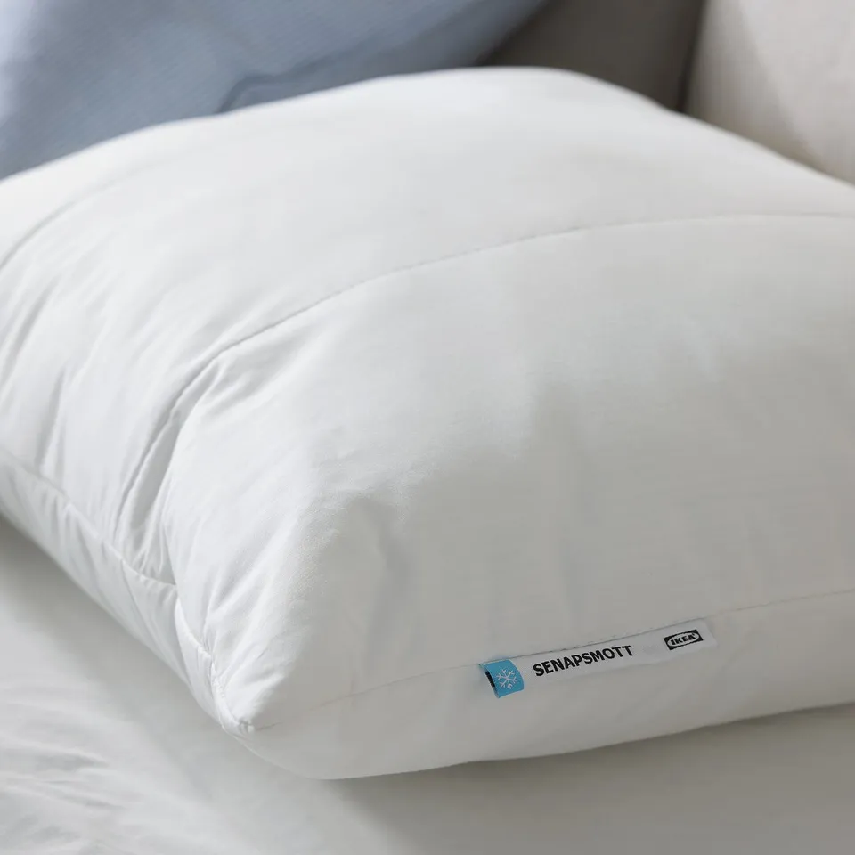 A white SENAPSMOTT pillow from IKEA. Its rectangular, made with a blend of recycled polyester and lyocell, offering cooling comfort for sleepers.