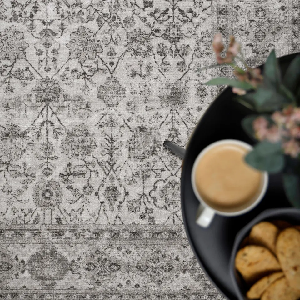 Elegant table setting with intricate patterned tablecloth, black tray holding coffee mug and cookies, accented by lush greenery.