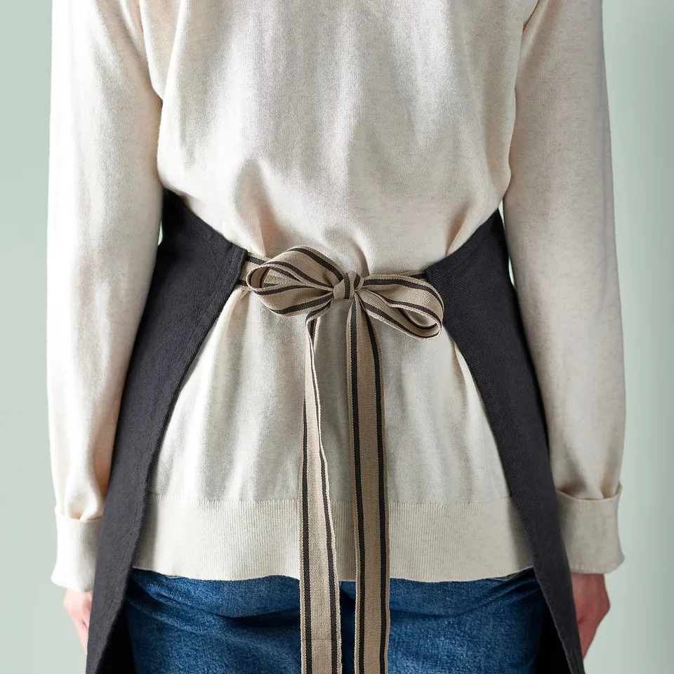Apron tied around waist with bow, featuring loops for kitchen tools and pockets for small items.