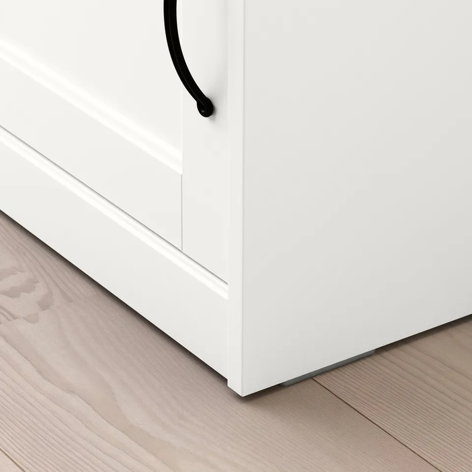 White cabinet with black handle on light wood floor. Clean, modern design visible.
