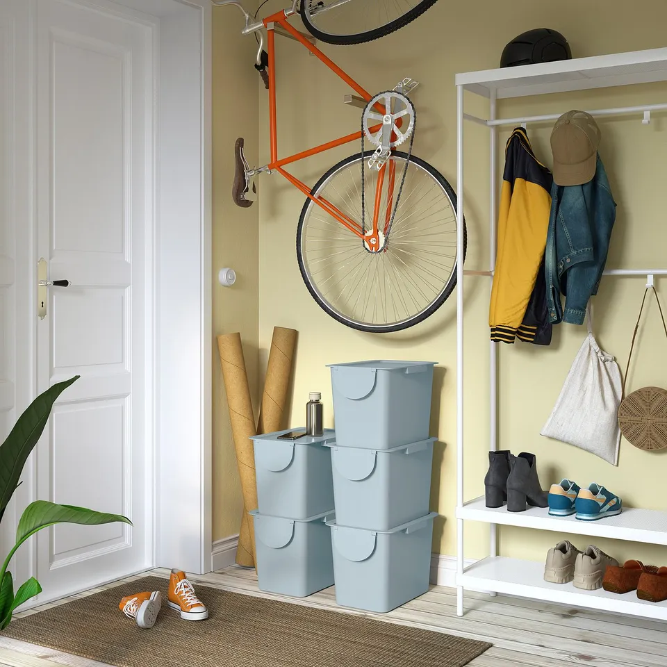 A bright entryway with an orange bike, blue bins, and white storage rack.