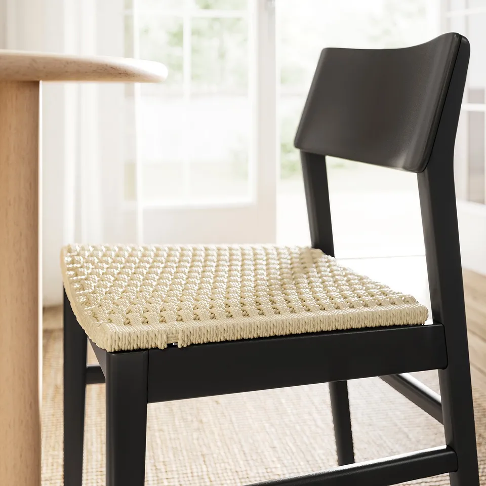Modern black chair with woven seat, near wooden table. Intricate, textured pattern offers comfort and style. Sleek backrest adds contemporary design.