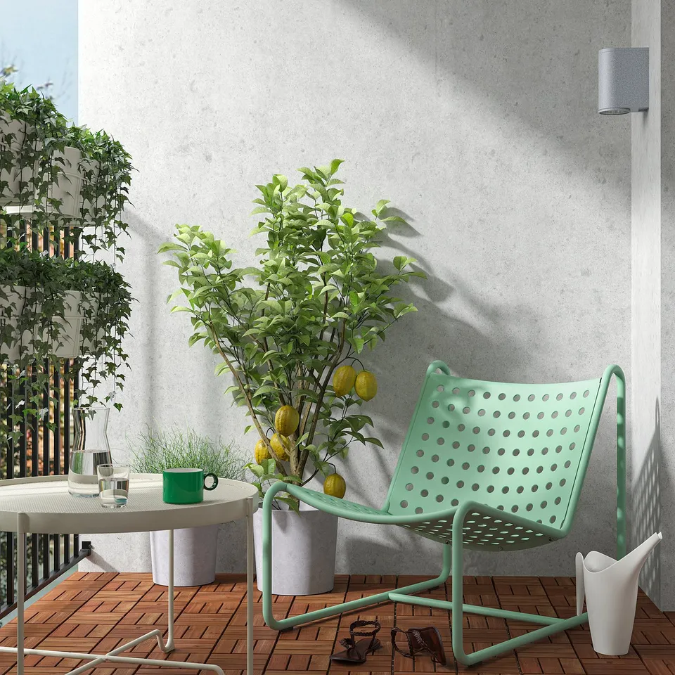Modern balcony with mint green SKOGSÖN chair, lemon tree, and round table. Chair made of metal with perforated seat, fits between wall and table.