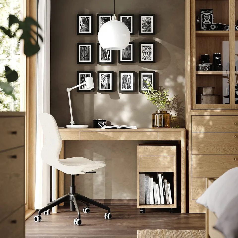 Modern home office with wooden desk, white chair, art, lamp, plant, books.
