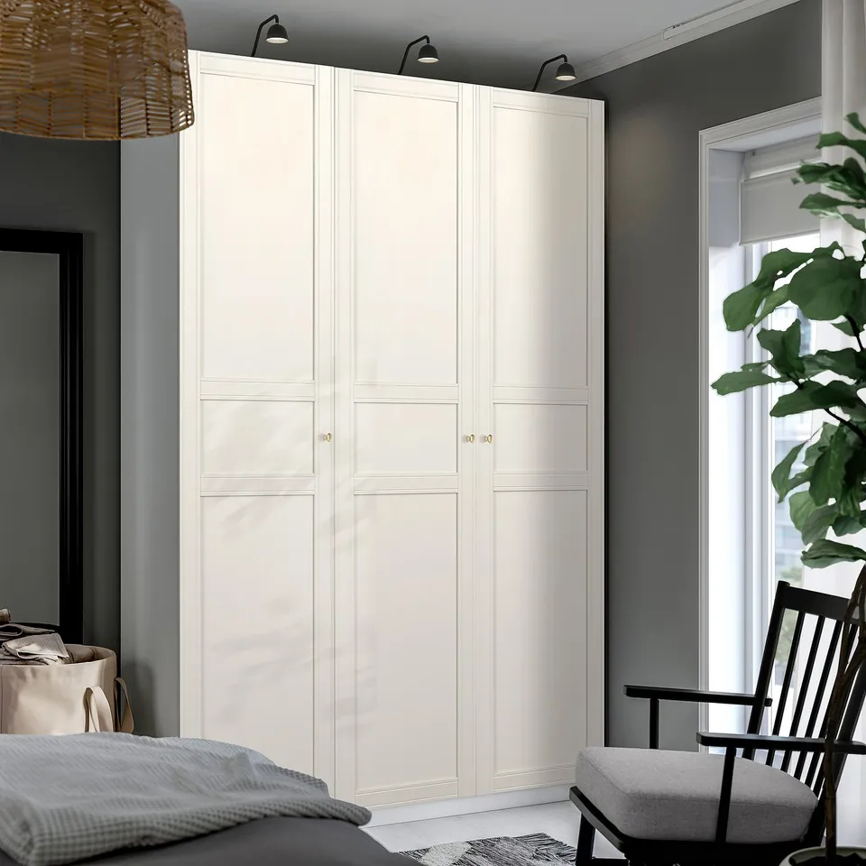 Minimalist bedroom with large white PAX wardrobe, sleek design, tall and wide, grey walls, modern chair, bed, and plant.