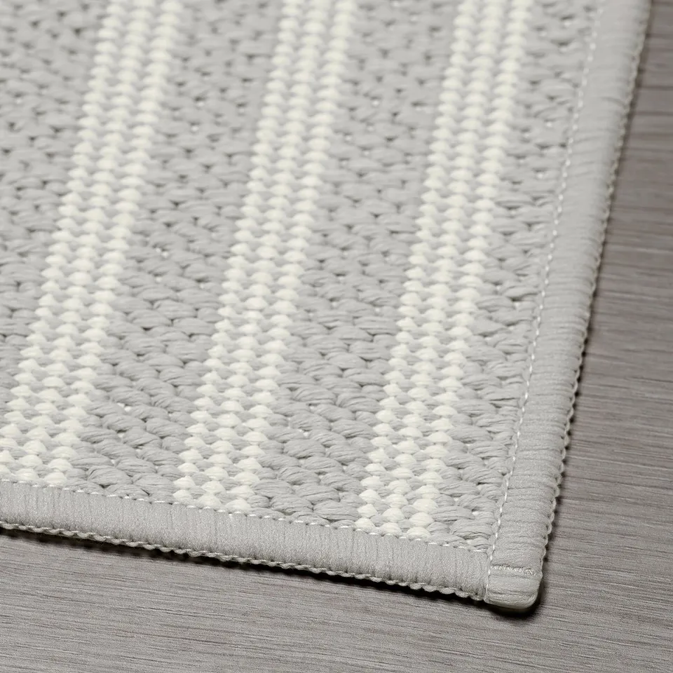 Close-up of a woven kitchen mat with intricate grey and white patterns, showcasing its textured quality and edge stitching.