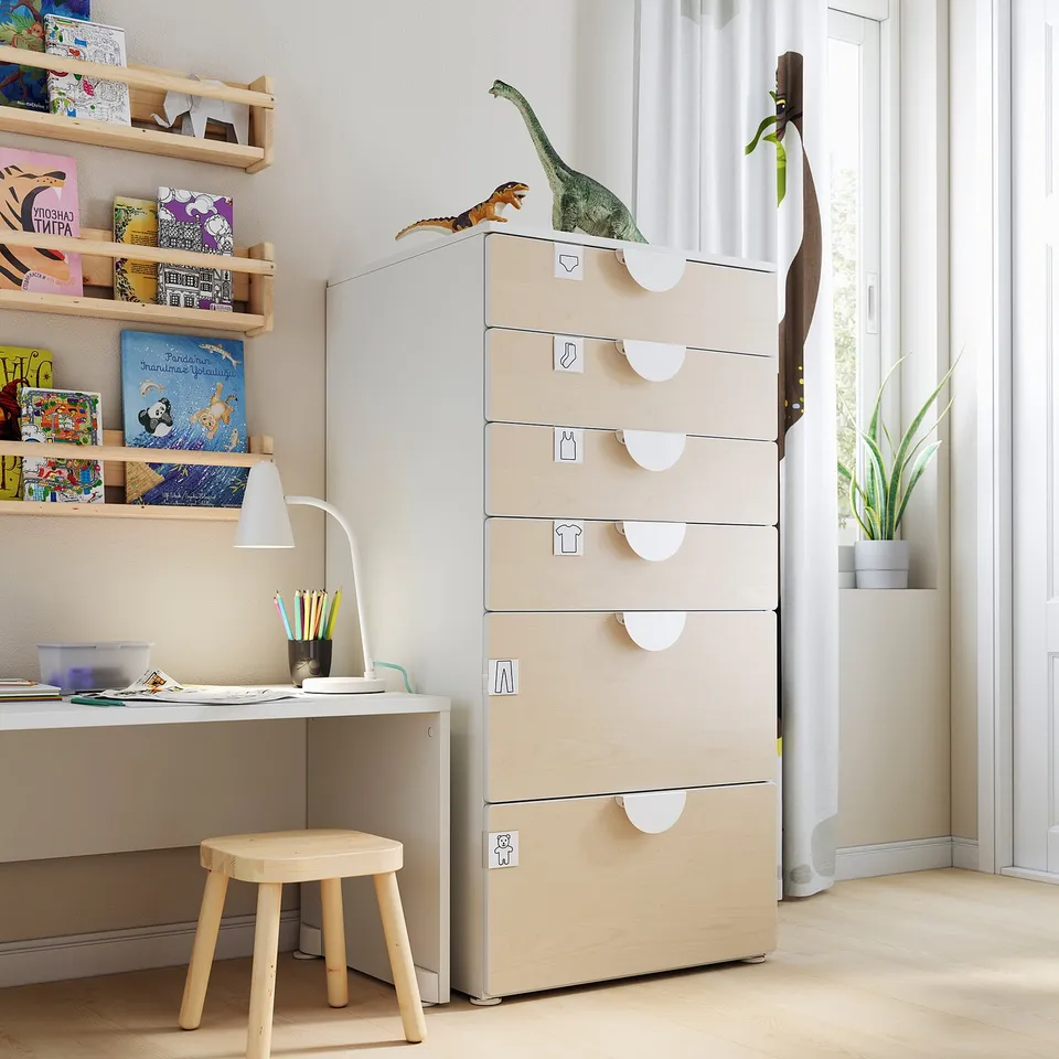 Childrens room with beige SMÅSTAD chest, drawers, desk, lamp, stools, dinosaur toys, books, and plant.