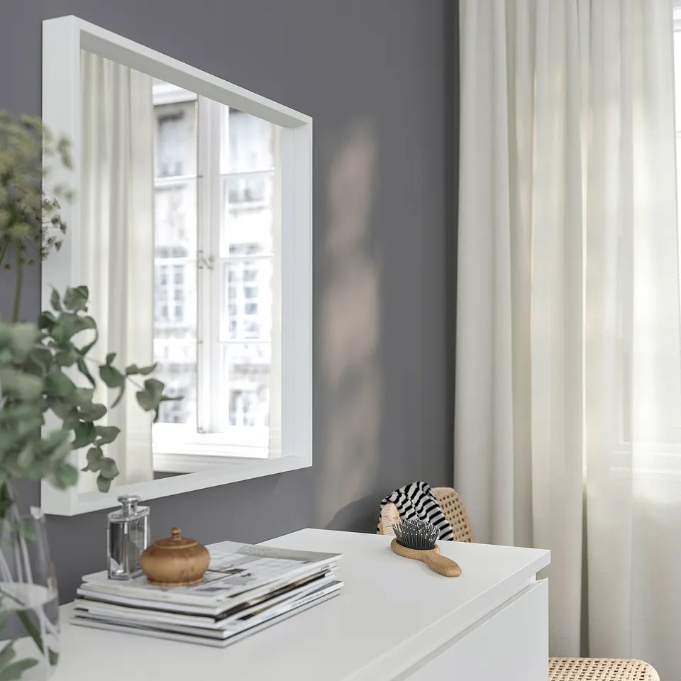 Minimalist white vanity with mirror, brush, and decor against grey wall.