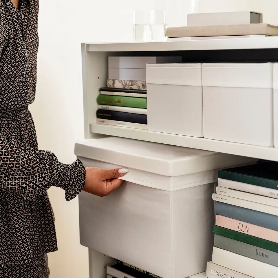 A person reaches for a fabric storage box in a shelf, demonstrating its easy access and organisation in a storage unit.