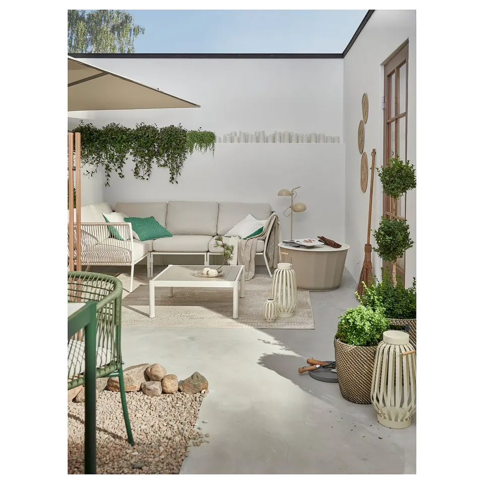 Modern outdoor patio with white SEGERÖN sofa, green chairs, and potted plants, creating a cosy relaxation space.