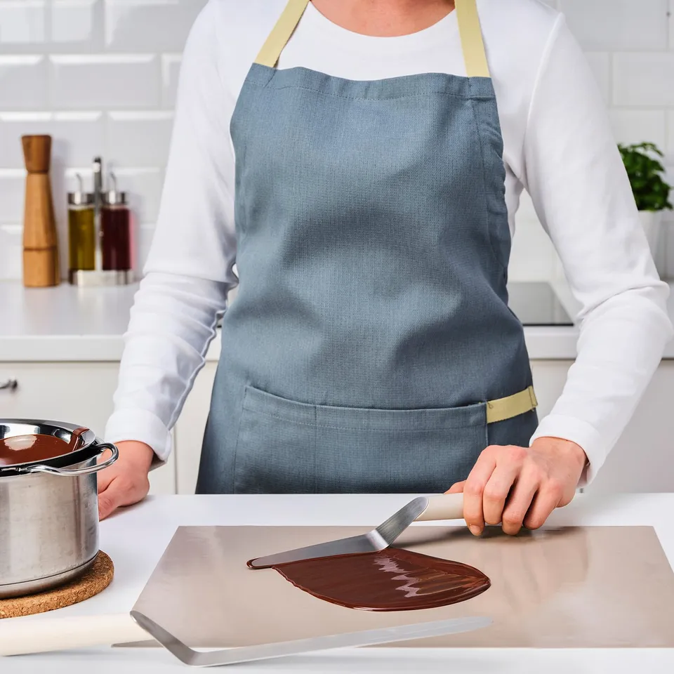 A chef uses an offset spatula to spread melted chocolate, demonstrating its use in baking.