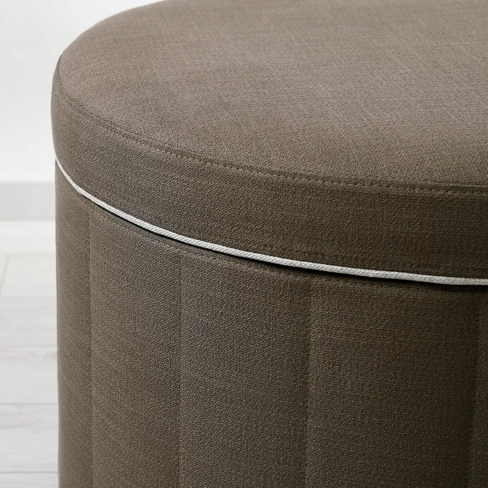 Close-up of a high-quality, round ottoman with sleek lines and piping detail, showing its sturdy fabric construction.