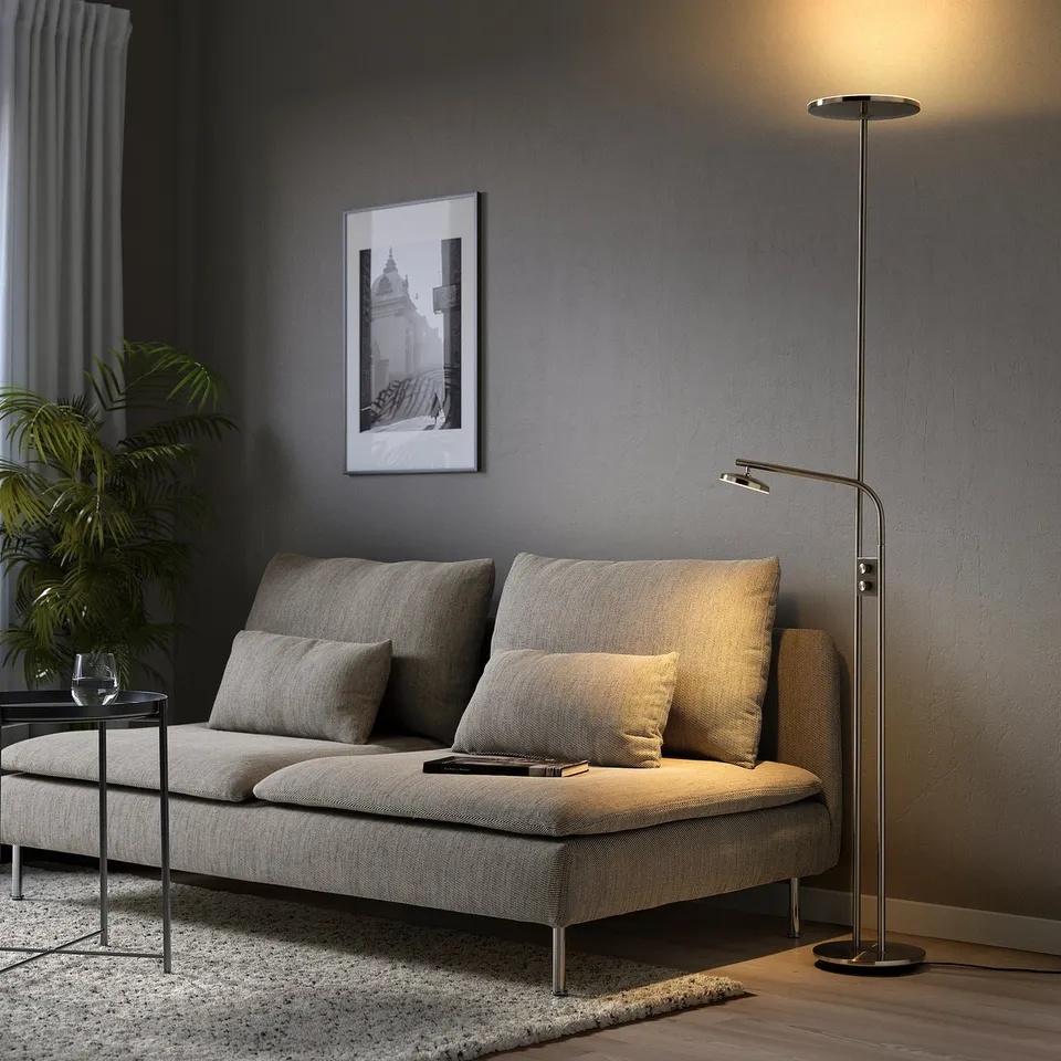 Modern living room with nickel floor lamp, grey sectional, plant, & black-white art.