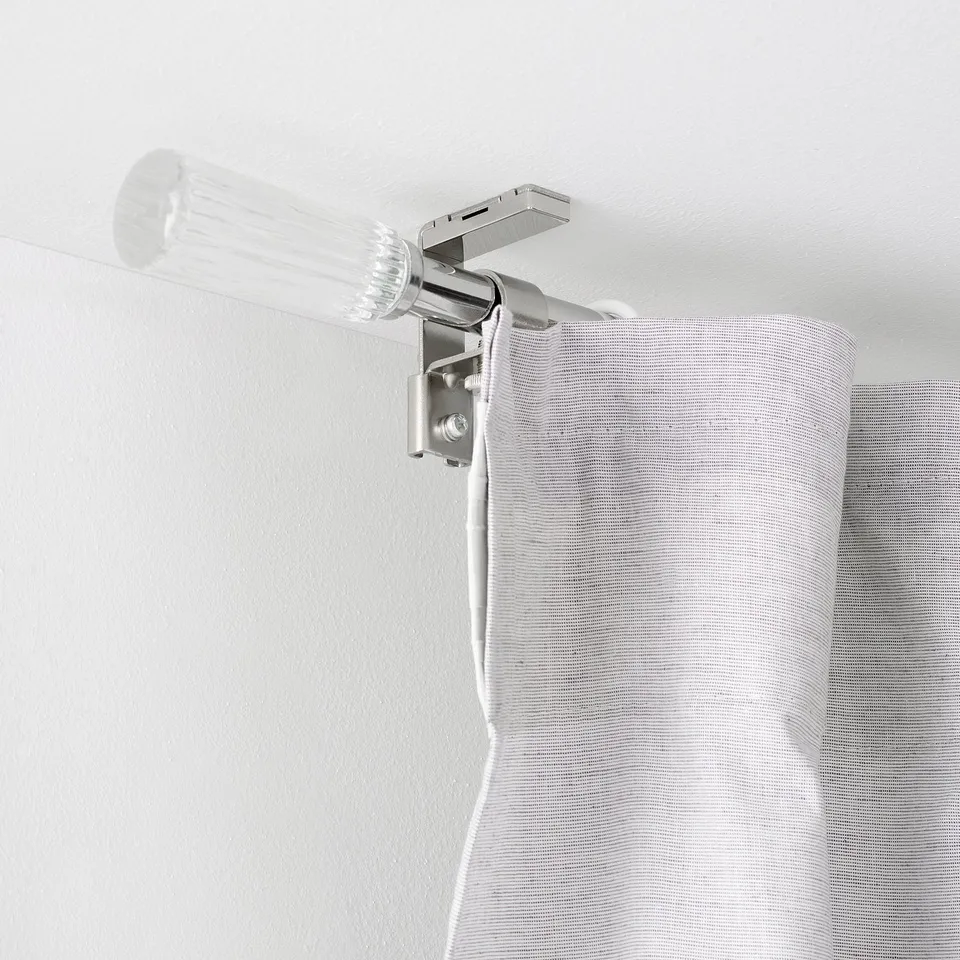 Clear curtain rod mounted near ceiling with white cord dangling, likely for automated curtain control.