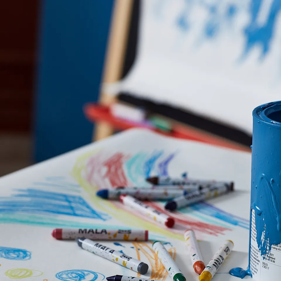 Colourful crayons labelled MÅLA, some used, with a blue cup and drawings. Safe for kids, promotes creativity.