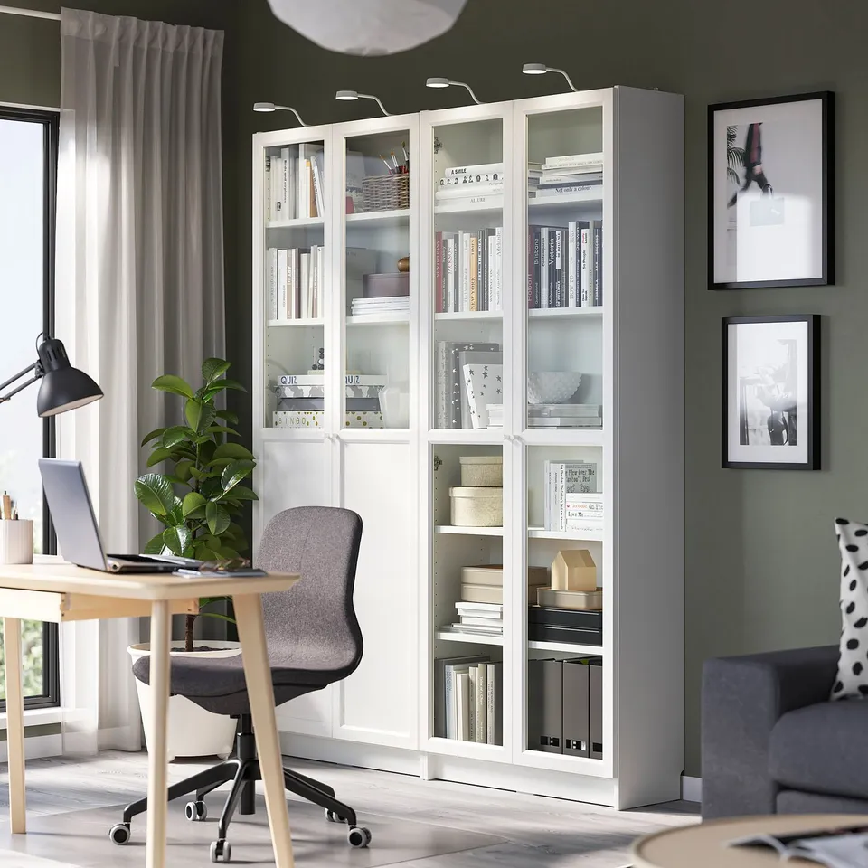 White BILLY bookcase with glass doors in a modern home office, surrounded by a desk, chair, and couch, showcasing its large size and sleek design.