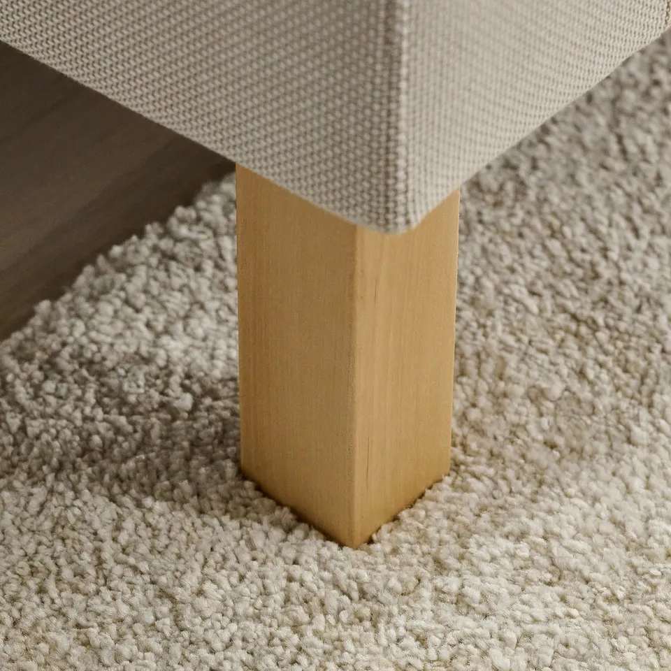 Close-up of sofa leg, polished, natural wood finish on textured carpet.