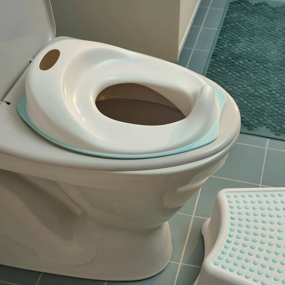 White toddler training toilet seat, shaped for children, with soft edges, sitting on a standard toilet, easy to remove and clean.