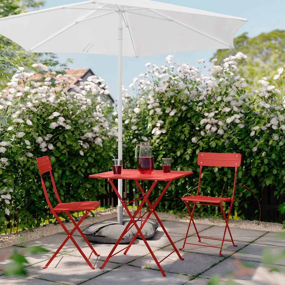Small red metal patio set with white umbrella, two chairs, and table, ideal for compact spaces.