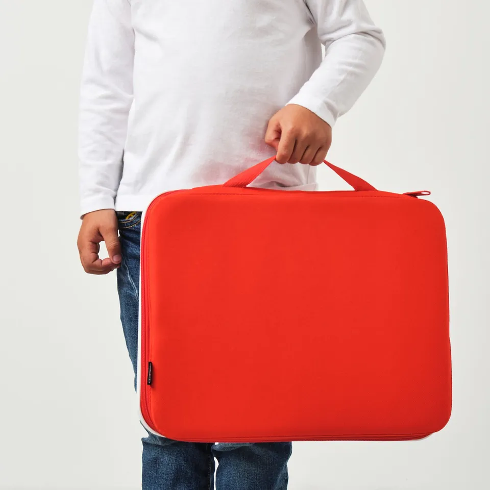 A person holding a bright red MÅLA drawing case. The case multiple pockets and a drawing board, ideal for carrying art supplies.
