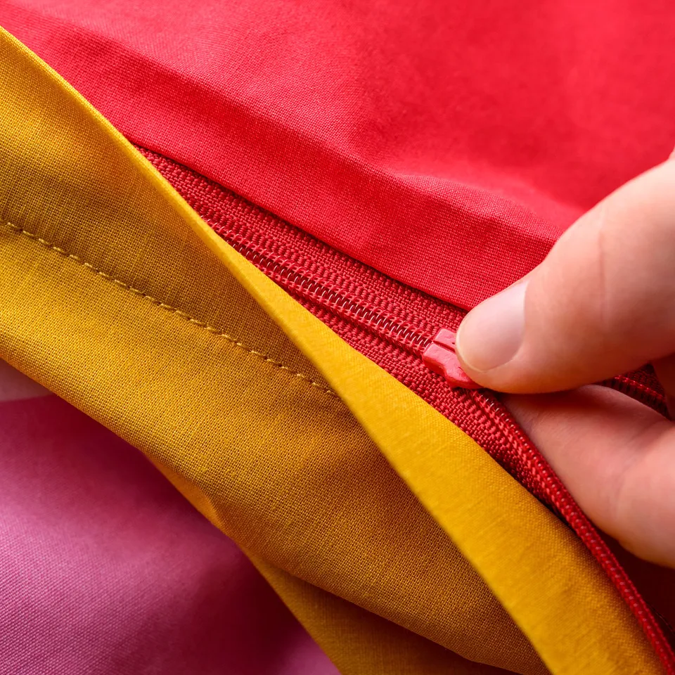 A hand zips a yellow and red duvet cover, showcasing a safe design without pull tabs.