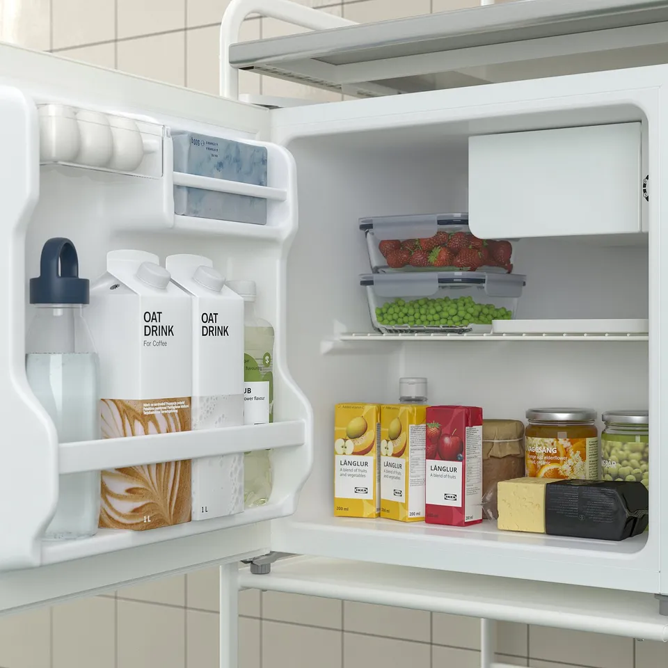 Open mini fridge displaying oat drinks, fruits, juices, and butter. White and well-organized.