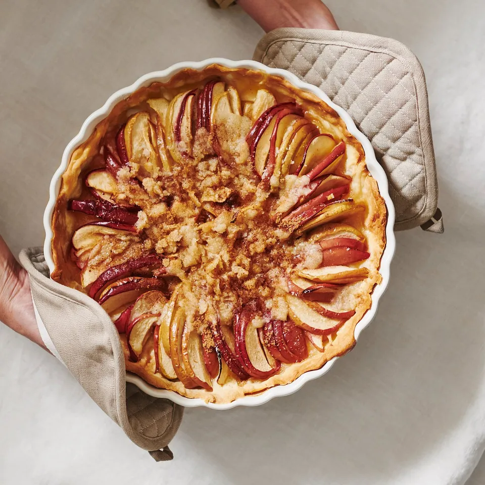 Person holding apple pie in scalloped dish with potholders.