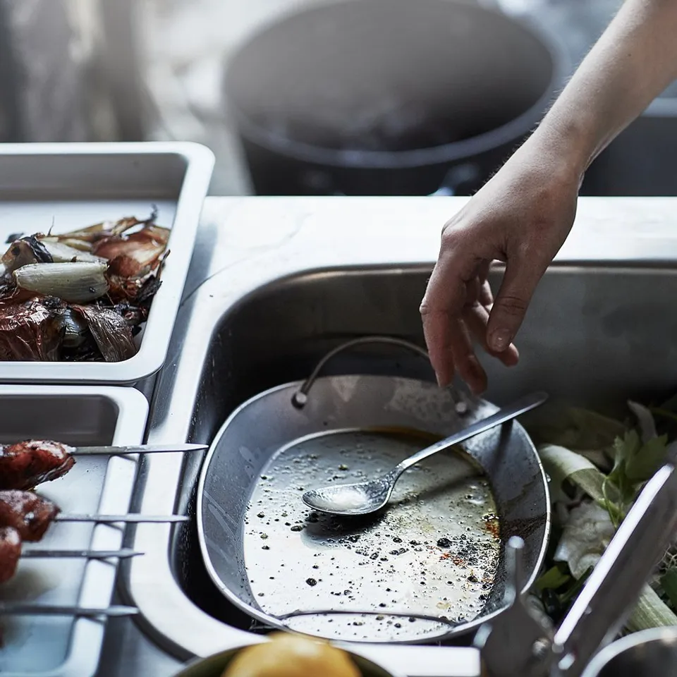 Cooking in kitchen with stainless sink and vegetables.