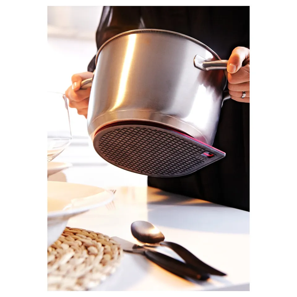 Person holding cookware with magnetic base on stand. Spoon and coaster on table.