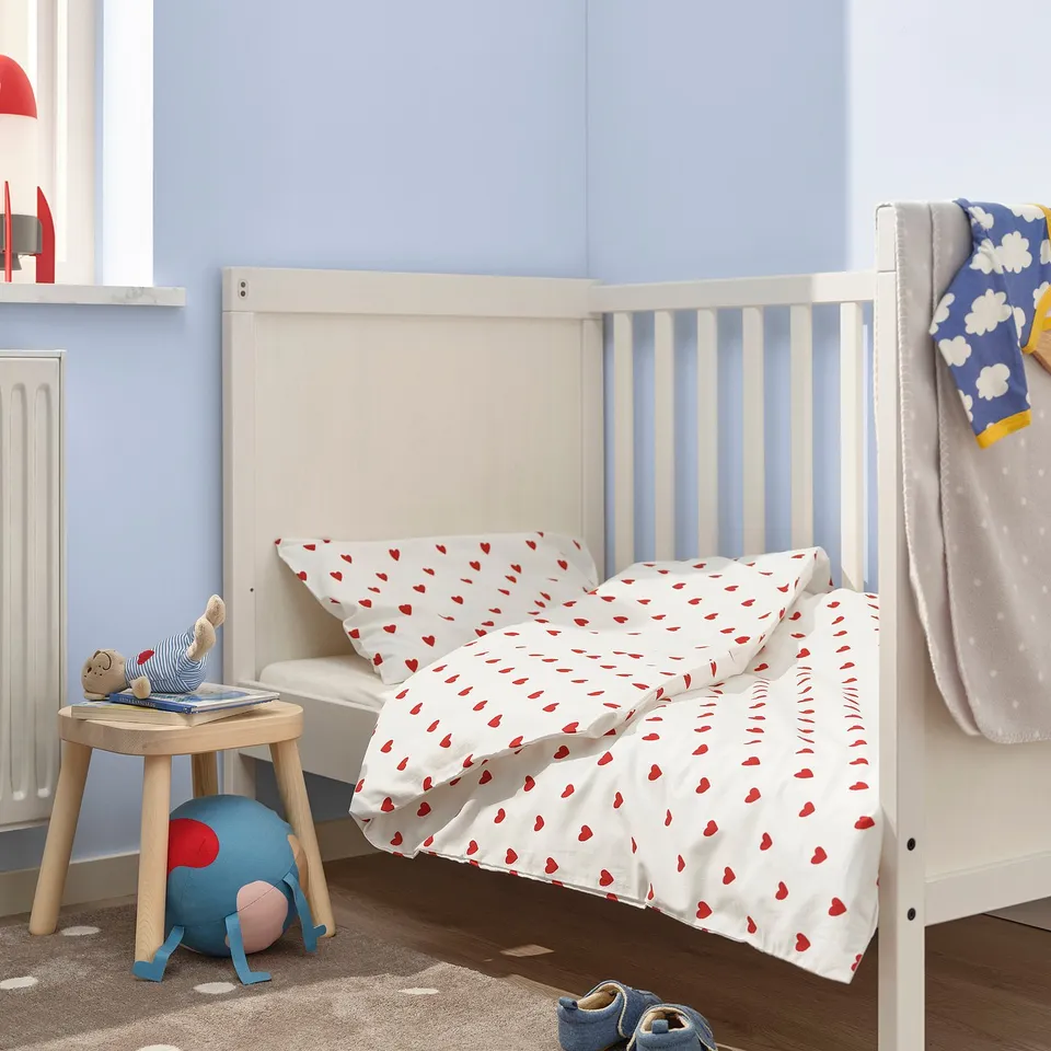 Baby duvet with red hearts on crib, cosy setting with toys and books.