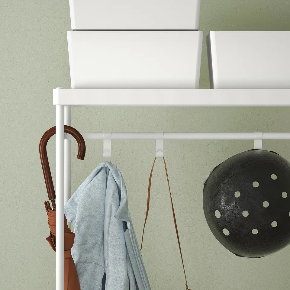 White MACKAPÄR coat rack with hooks, holding umbrella and light blue clothing. Above are storage boxes.