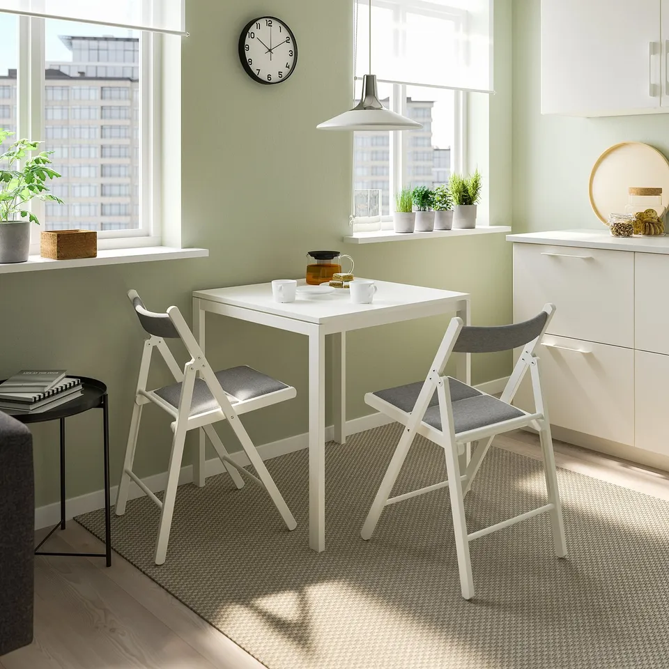 Cosy dining nook with white chair, green table, plants, and clock. Natural light.