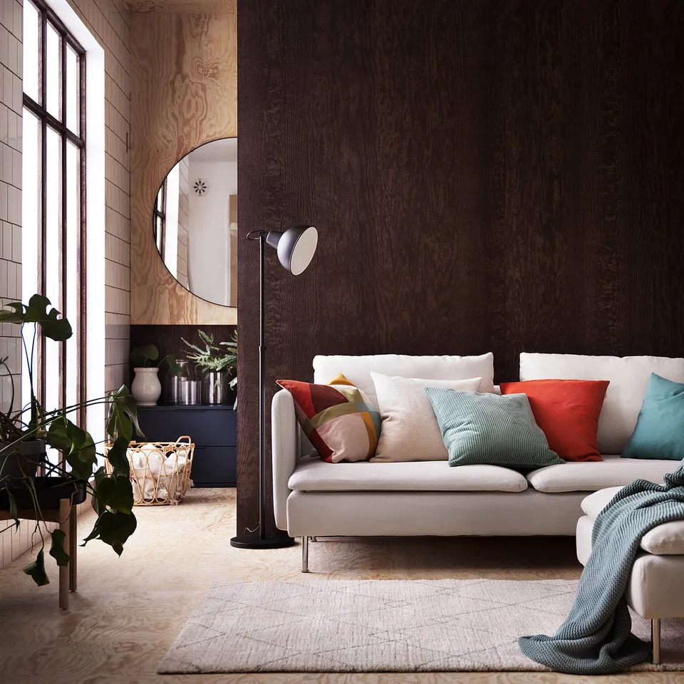 Modern living room with white sofa, colourful pillows, wooden textures, and a circular mirror. A berber-inspired rug and indoor plants add decor.