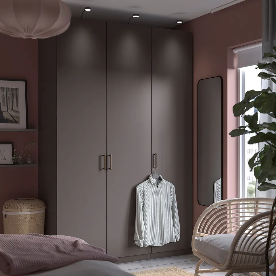 Modern bedroom with grey PAX wardrobe, pink walls, hanging shirt, and wicker chair.