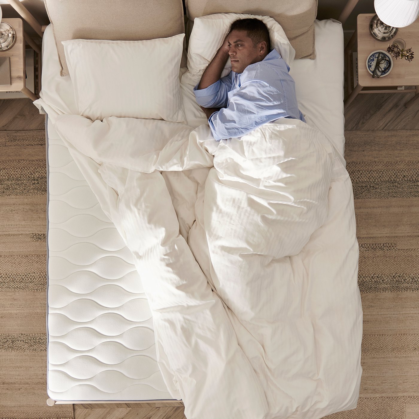 Person sleeps in bedroom on white VÅGSTRANDA mattress, blue shirt.
