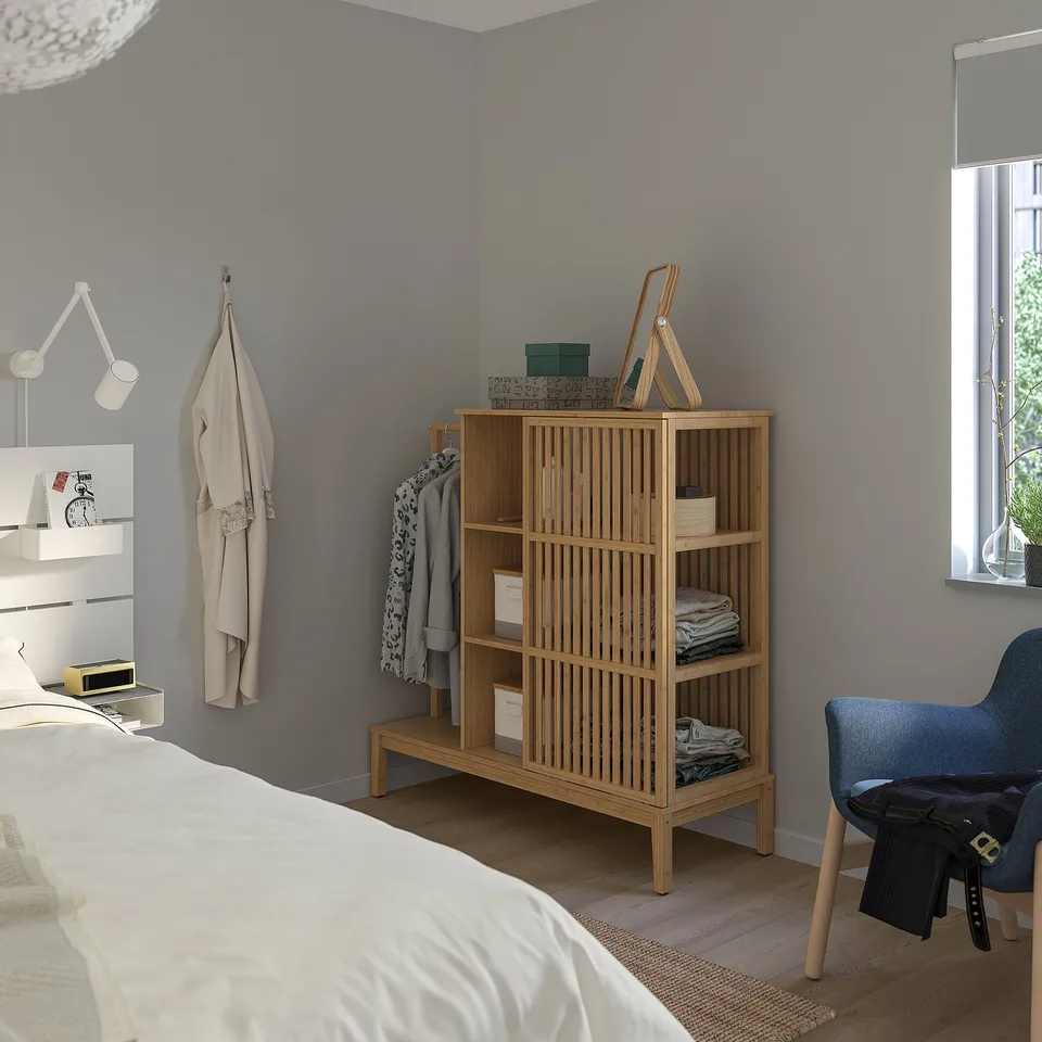 Modern bedroom with grey walls, light wood floor. Bamboo wardrobe, blue chair, white bed.