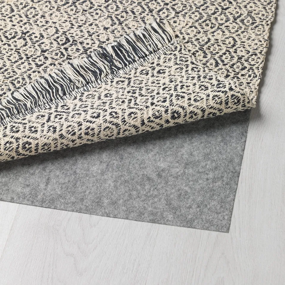 A grey leopard-print rug is shown rolled up on a light wooden floor, revealing its dark grey backside.