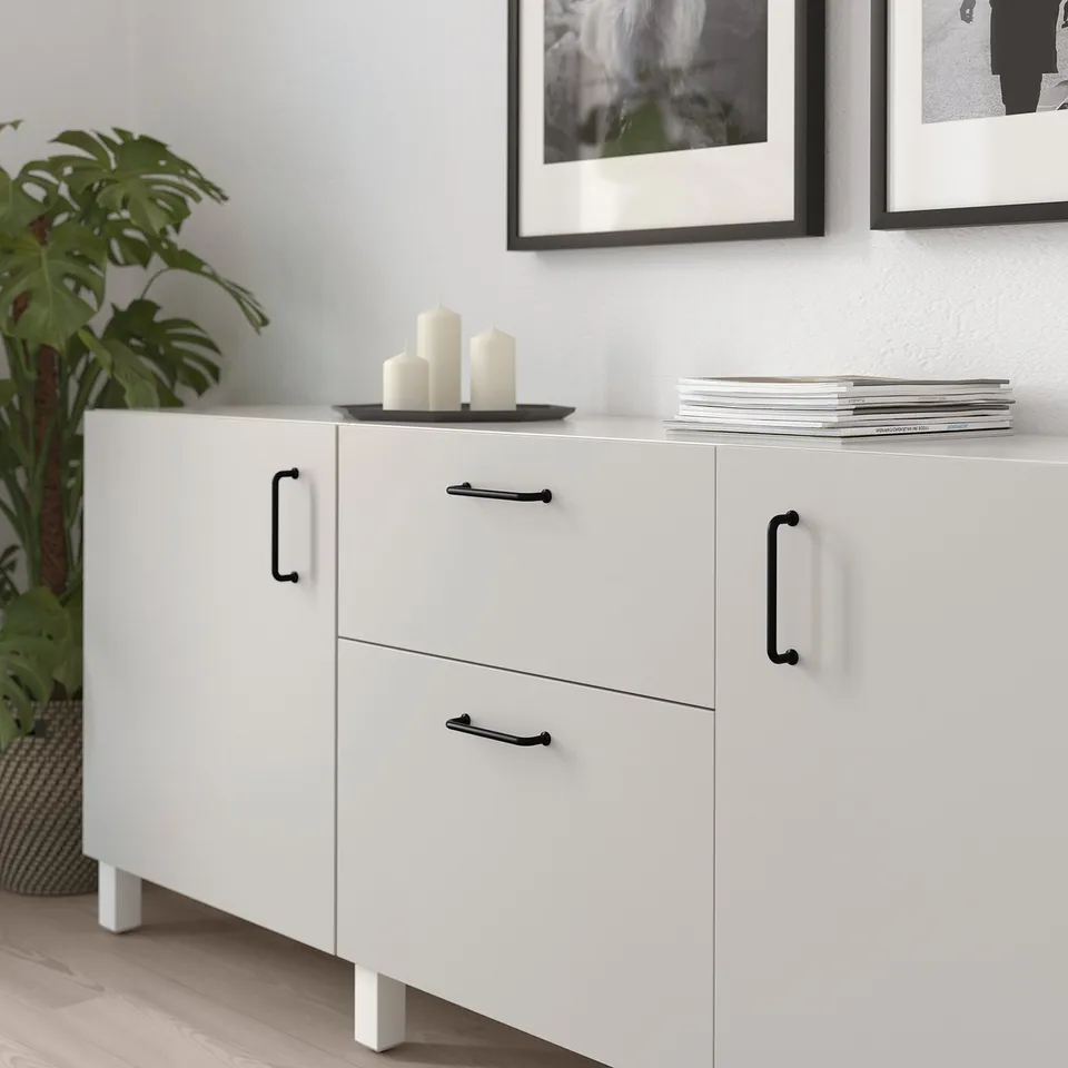White storage cabinet with black handles, featuring drawers, doors, and magazine storage on top, decorated with white candles.