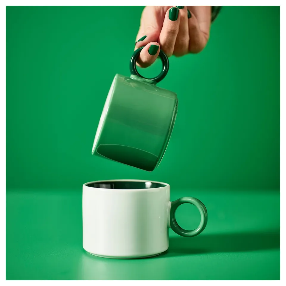 A hand holding green and white mugs with contrasting handles.