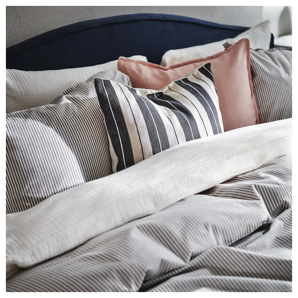 Cosy, striped cushions on a bed. Light beige and dark grey stripes, soft texture, rectangular shape.