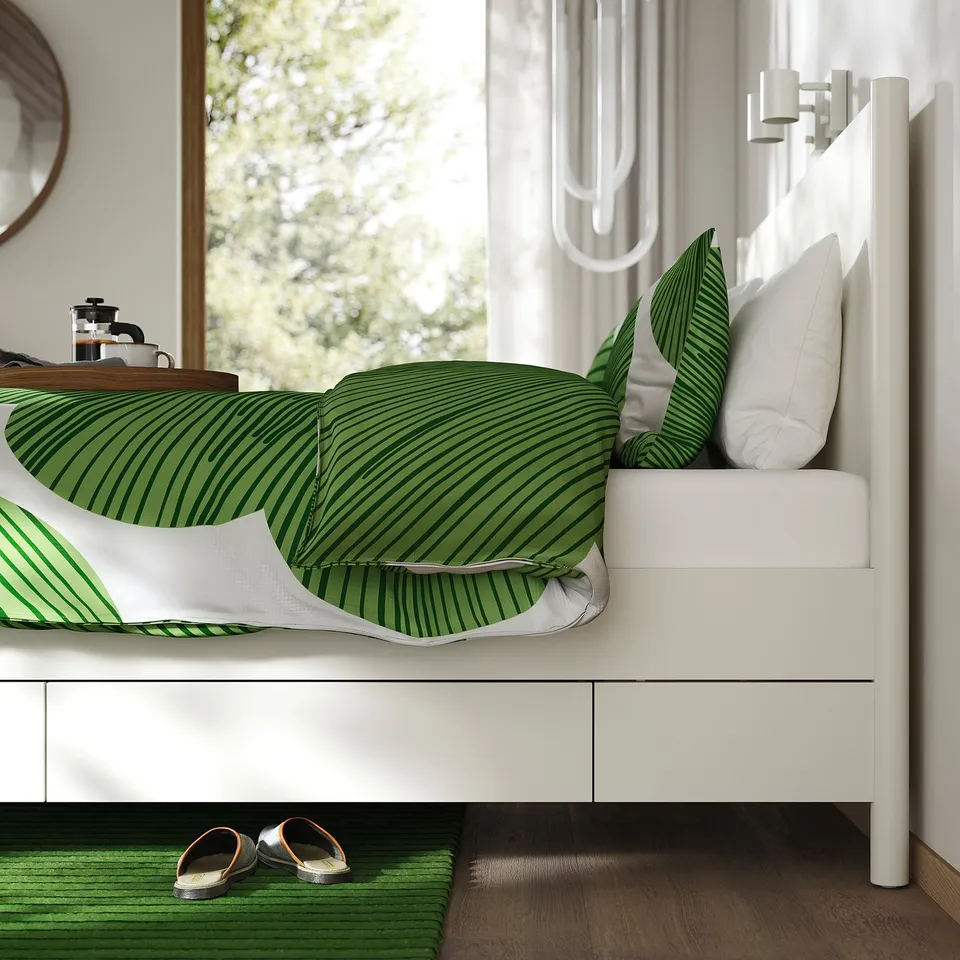 A white TONSTAD bed with green patterned pillows and white drawers, showcasing under-bed storage and a minimalist design.